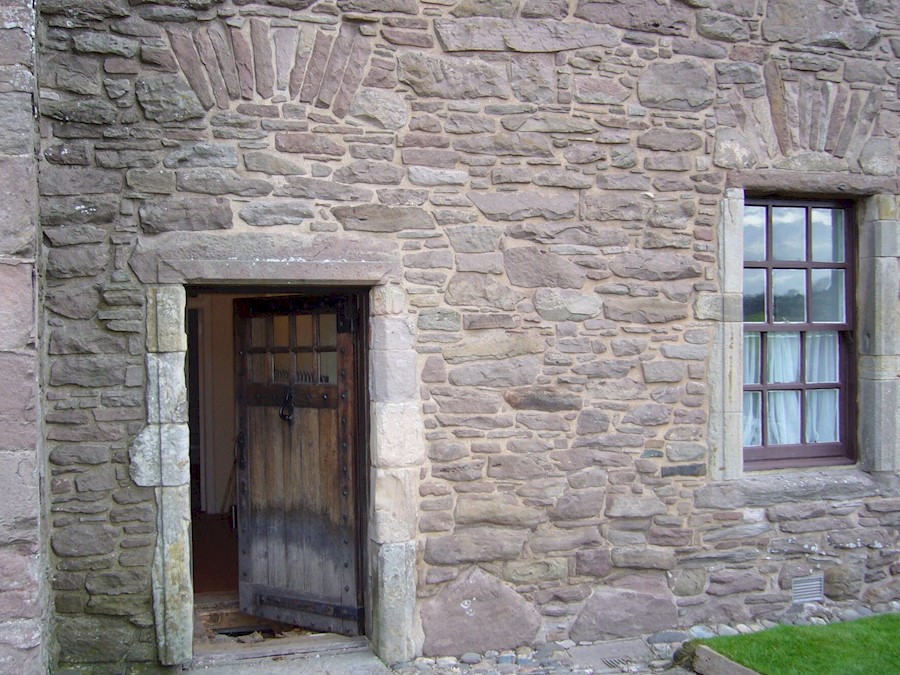 A timber door and window set into the side of a historic castle wall, made up of many intricate stones and shaped bricks.