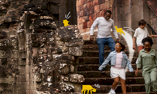 4 people running down stairs in a ruinness castle with yellow lambs superimposed on the picture