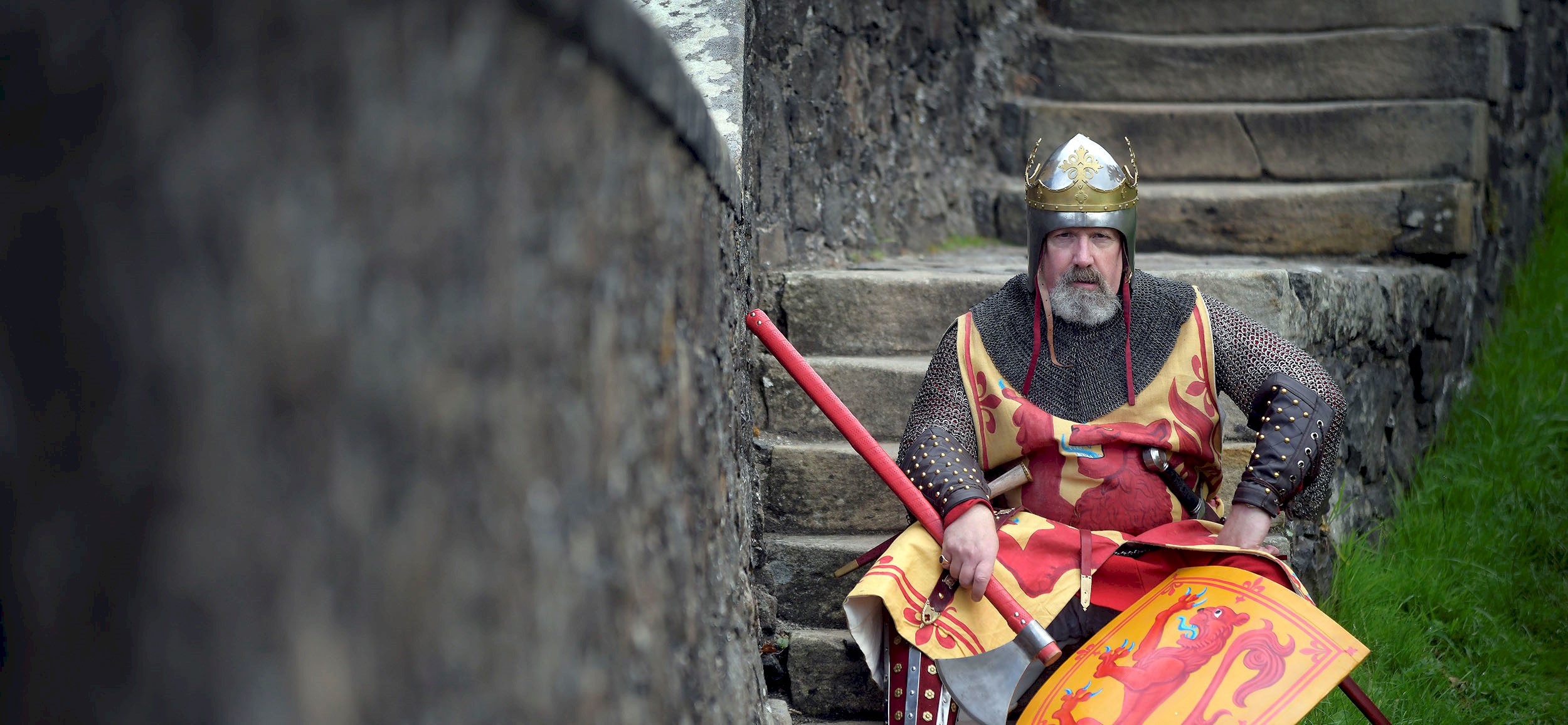 A costumed performer in chain mail holding a shield looking stern