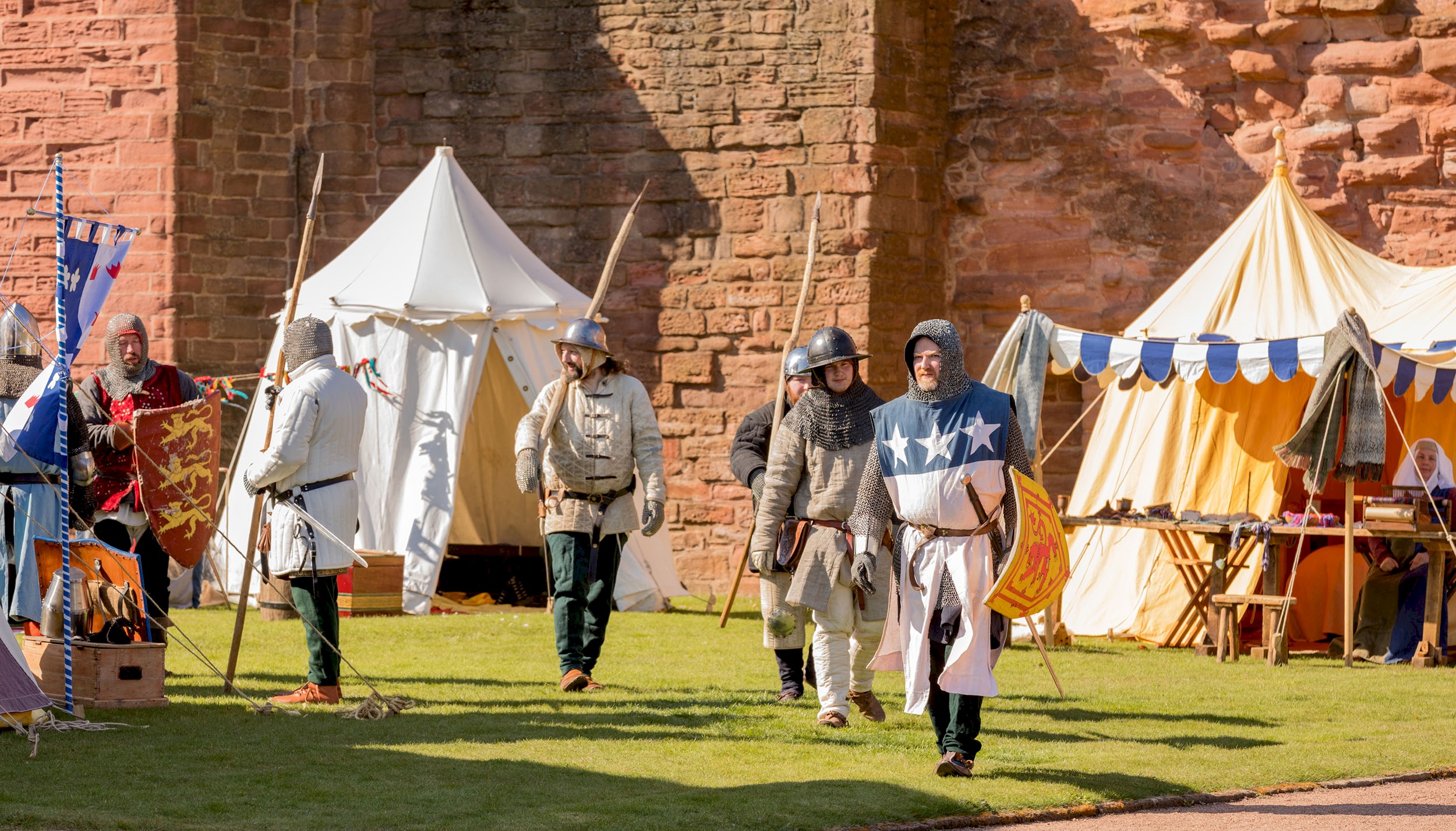 Costumed performers walking around a camp in the grounds of a castle 