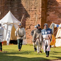 Costumed performers walking around a camp in the grounds of a castle