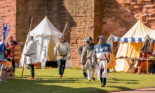Costumed performers walking around a camp in the grounds of a castle 