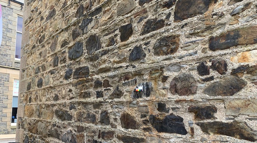 A traditional stone wall of a building. The building is pointed with lime and there's a small card placed on the wall to help identify the lime type.