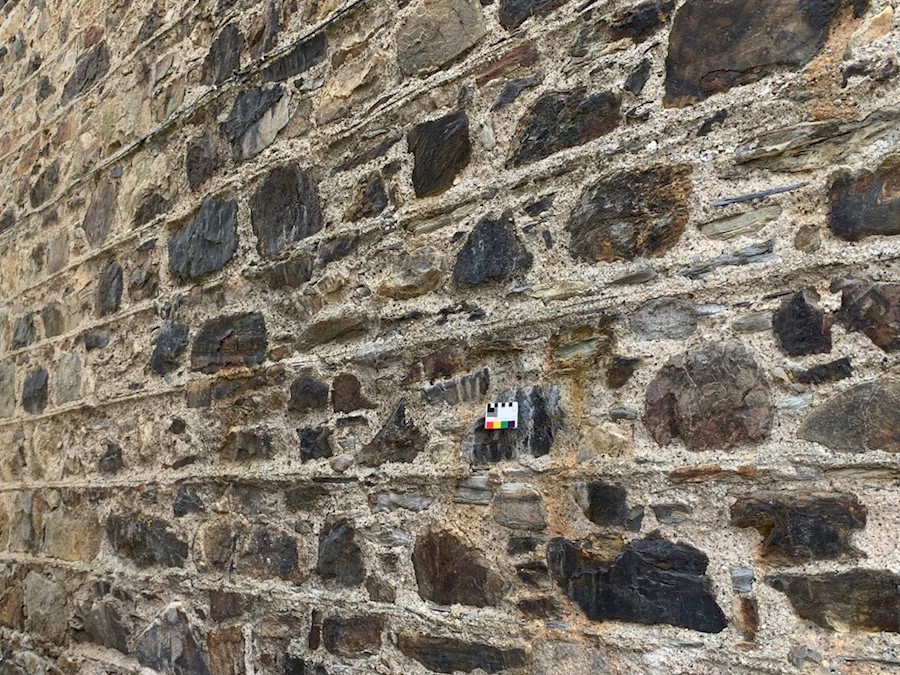 A traditional stone wall of a building. The building is pointed with lime and there's a small card placed on the wall to help identify the lime type.