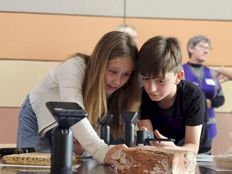 Two children examining building materials like brick and stone using scientific equipment