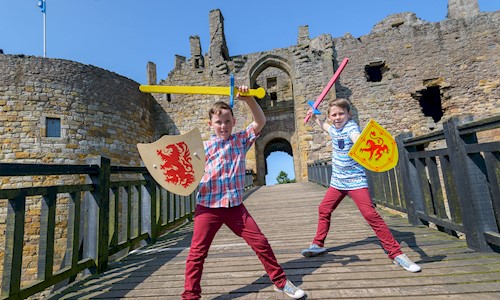 Two boys on Dirleton Castle drawbridge holding toy swords & shields