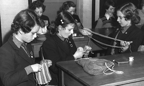 A black and white image of children in uniform in a class knitting 