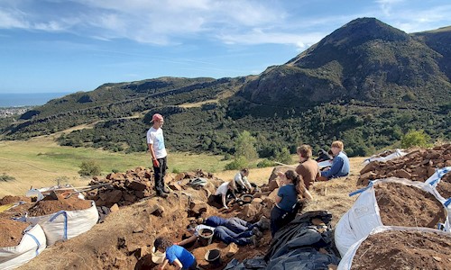 People doing an archaeological dig with beautiful blue sky and green hills