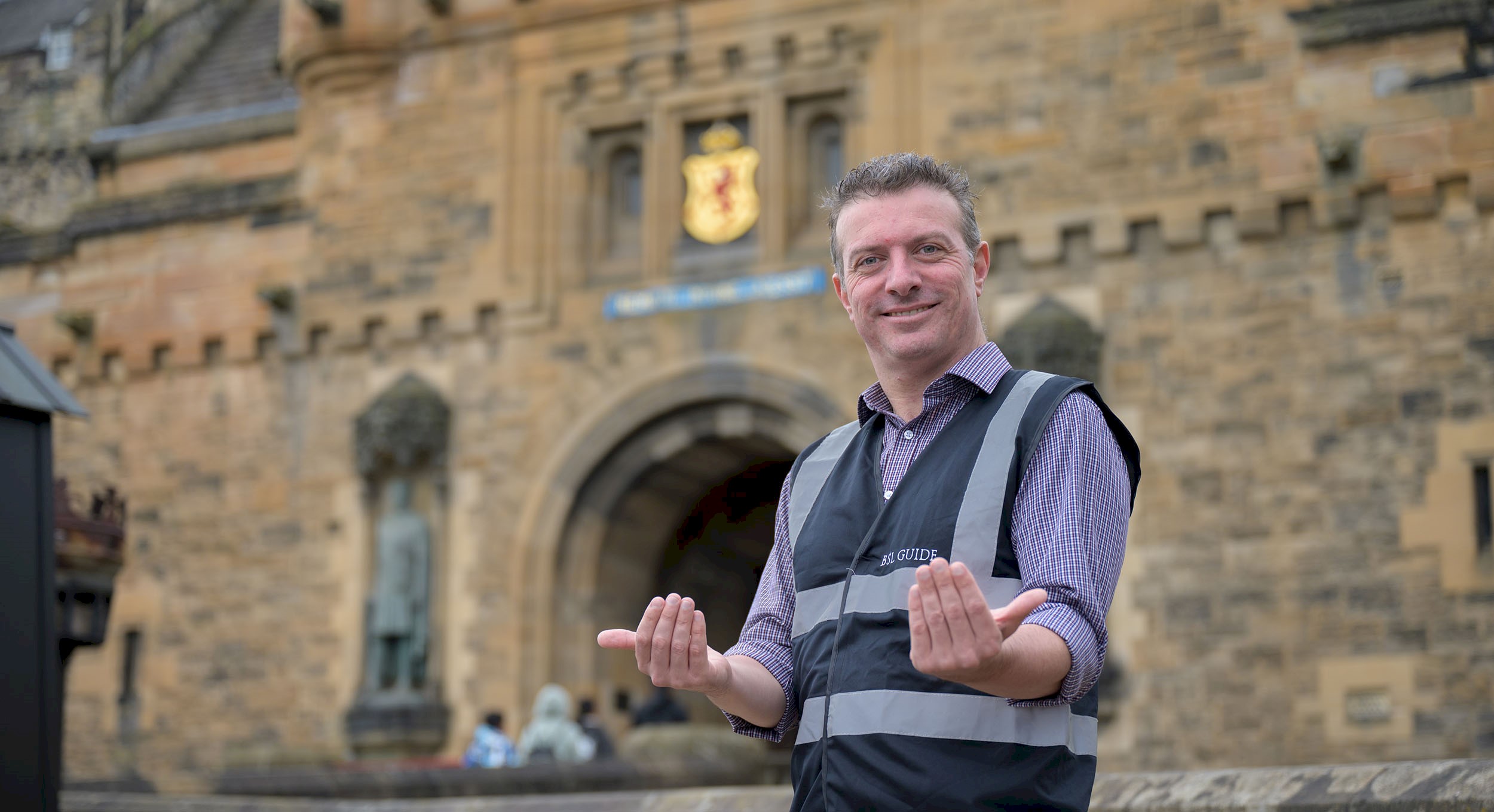 ISL guide Gordon Hay smiling and gesturing with his hands to welcome you to Edinburgh Castle
