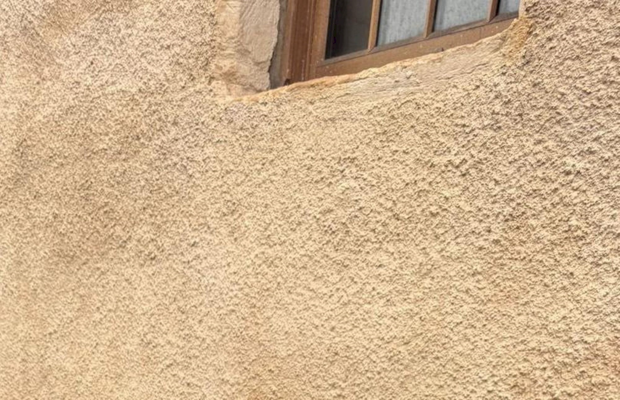 A light orange / yellow lime harled wall on a building with a brown window 