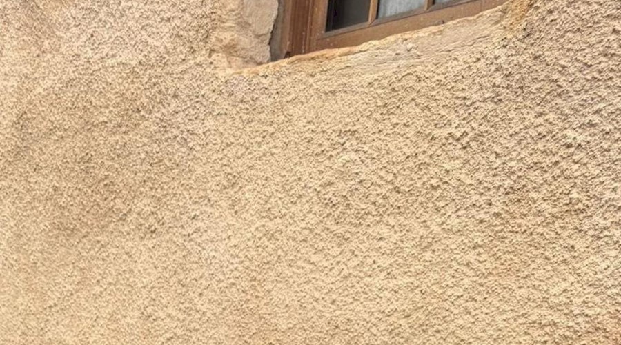 A light orange / yellow lime harled wall on a building with a brown window 