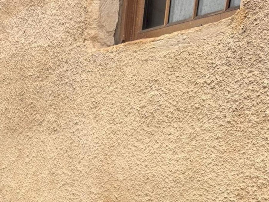 A light orange / yellow lime harled wall on a building with a brown window 