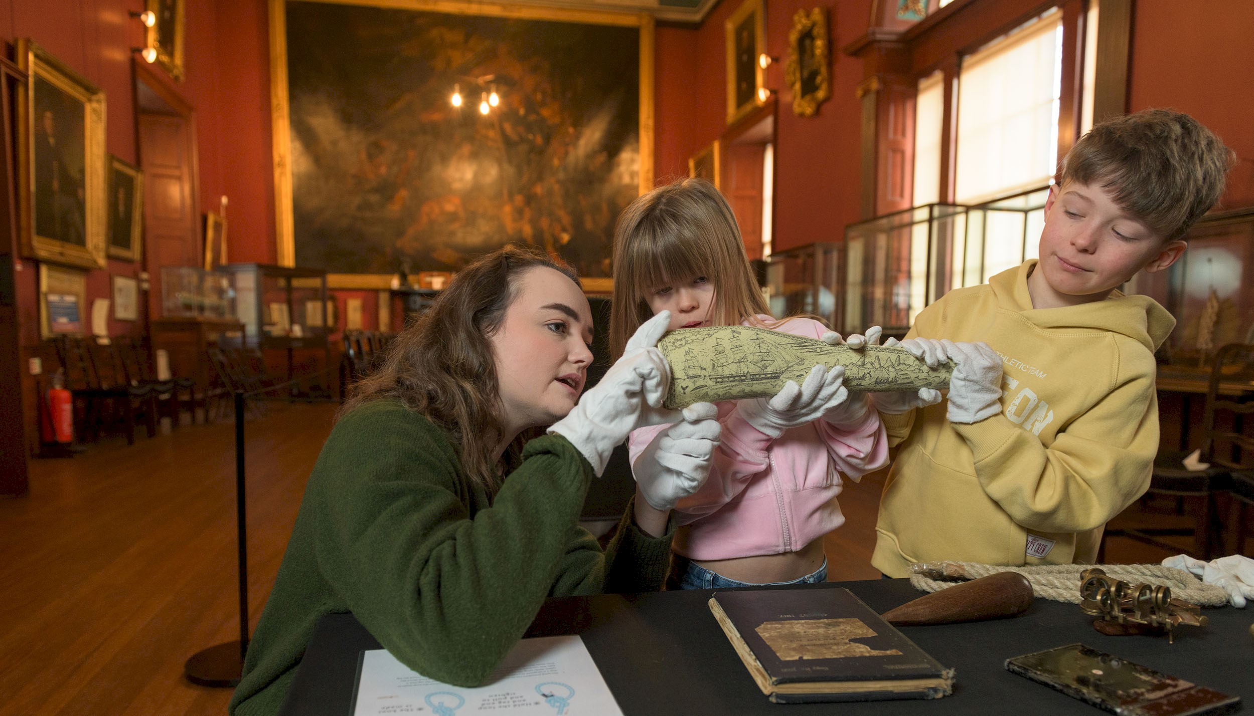 A woman kneeling down with two children looking at objects in Trinity House