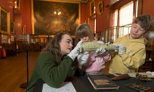 A woman kneeling down with two children looking at objects in Trinity House