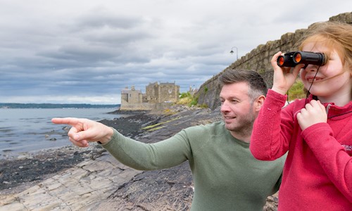 Visitors on the shore at Blackness using binoculars to enjoy the view, blackness castle in the background