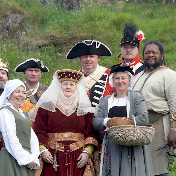A group of costumed performers in different period costumes standing on a grassy hill 