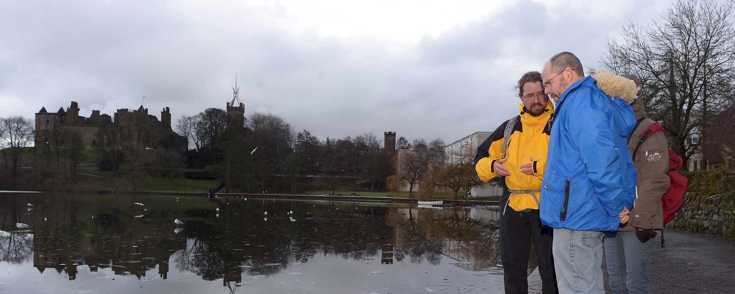 A Historic Scotland Ranger talking to two people by a loch with a palace in the background