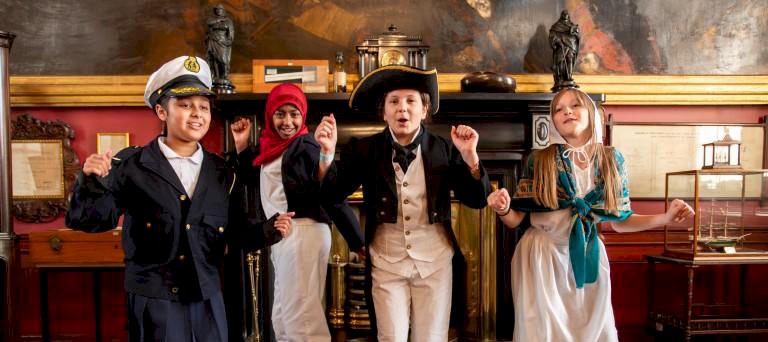 Children dressed up in maritime regalia smiling with their hands in the air