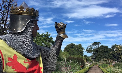 Man dressed as Robert the Bruce with Dirleton Castle Gardens behind him