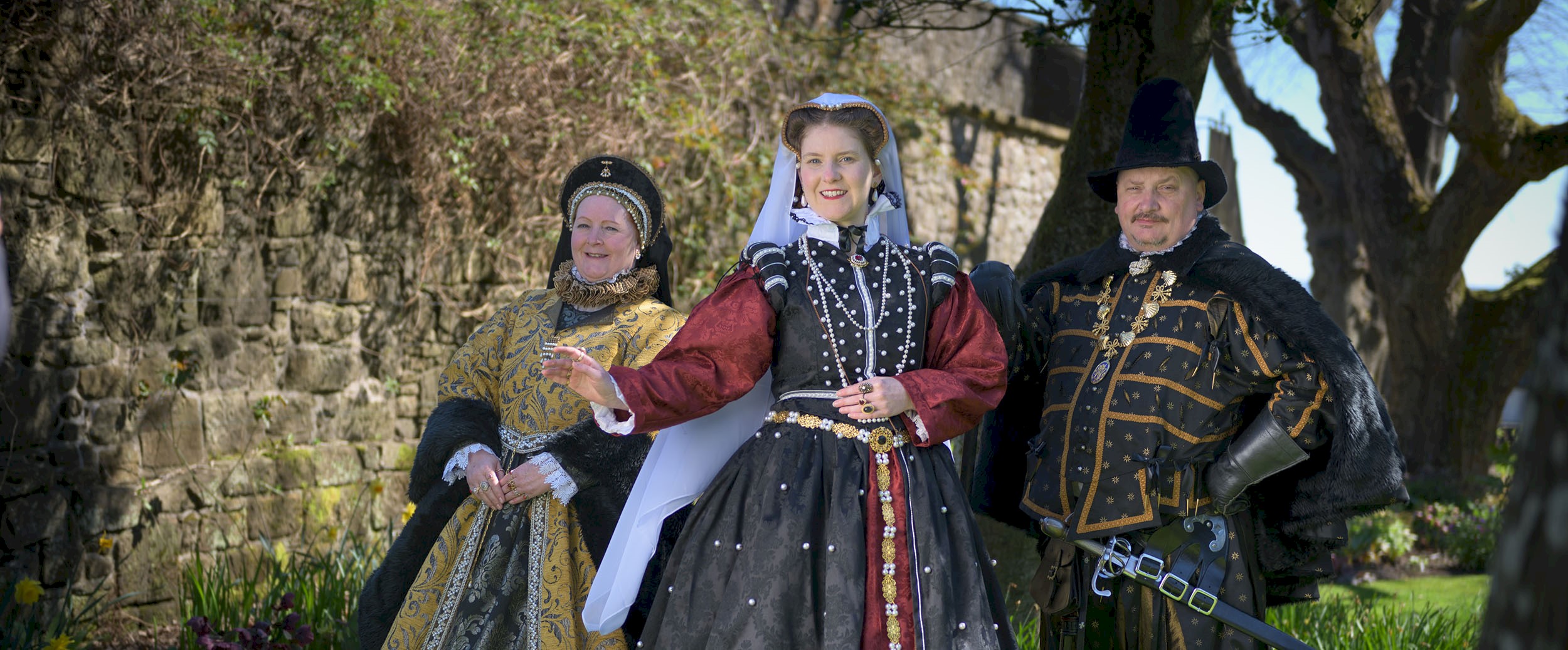 Three people in period costume surrounded by trees on a bright sunny day