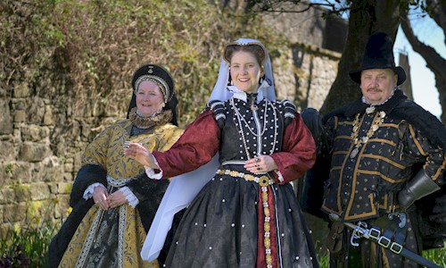 Three people in period costume surrounded by trees on a bright sunny day