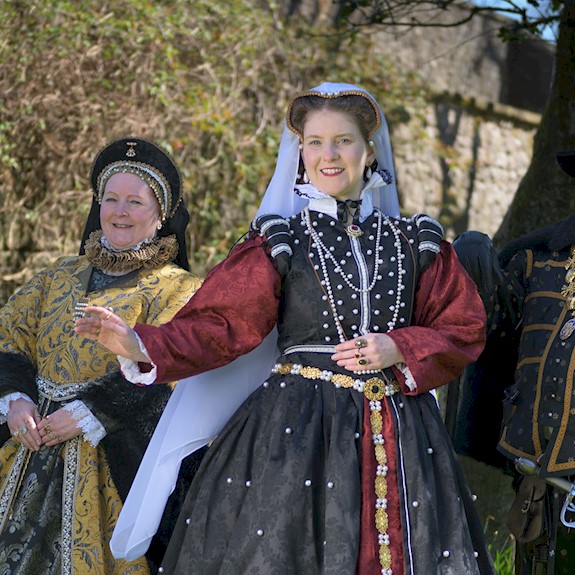 Three people in period costume surrounded by trees on a bright sunny day