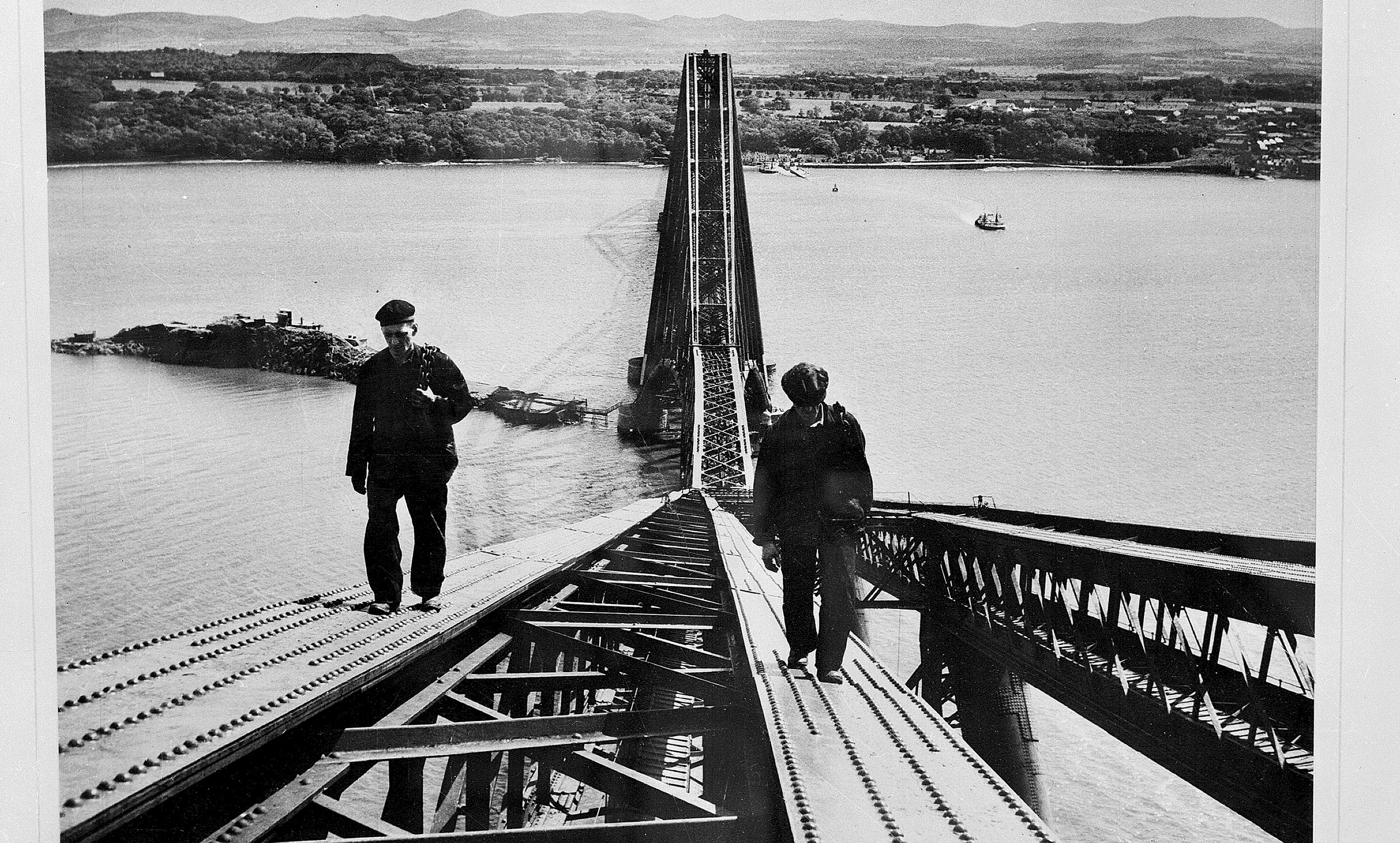 A black and white image of two men walking up the Forth Bridge 