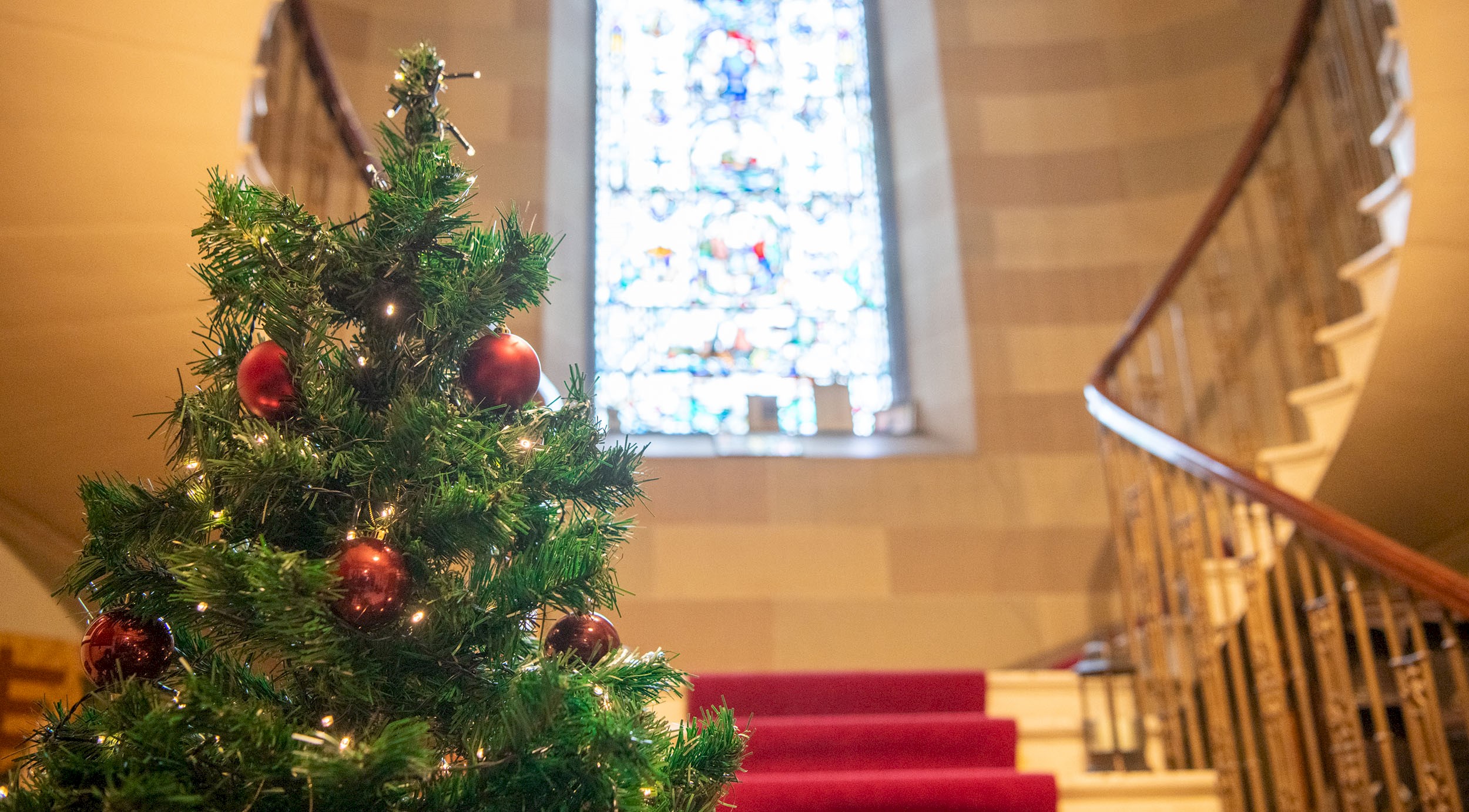A beautiful stair case with an imposing stain glass window and Christmas Tree
