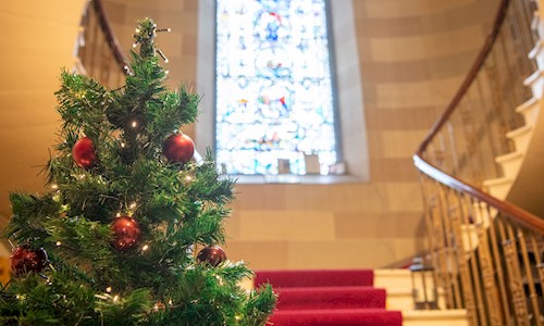 A beautiful stair case with an imposing stain glass window and Christmas Tree