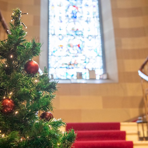 A beautiful stair case with an imposing stain glass window and Christmas Tree