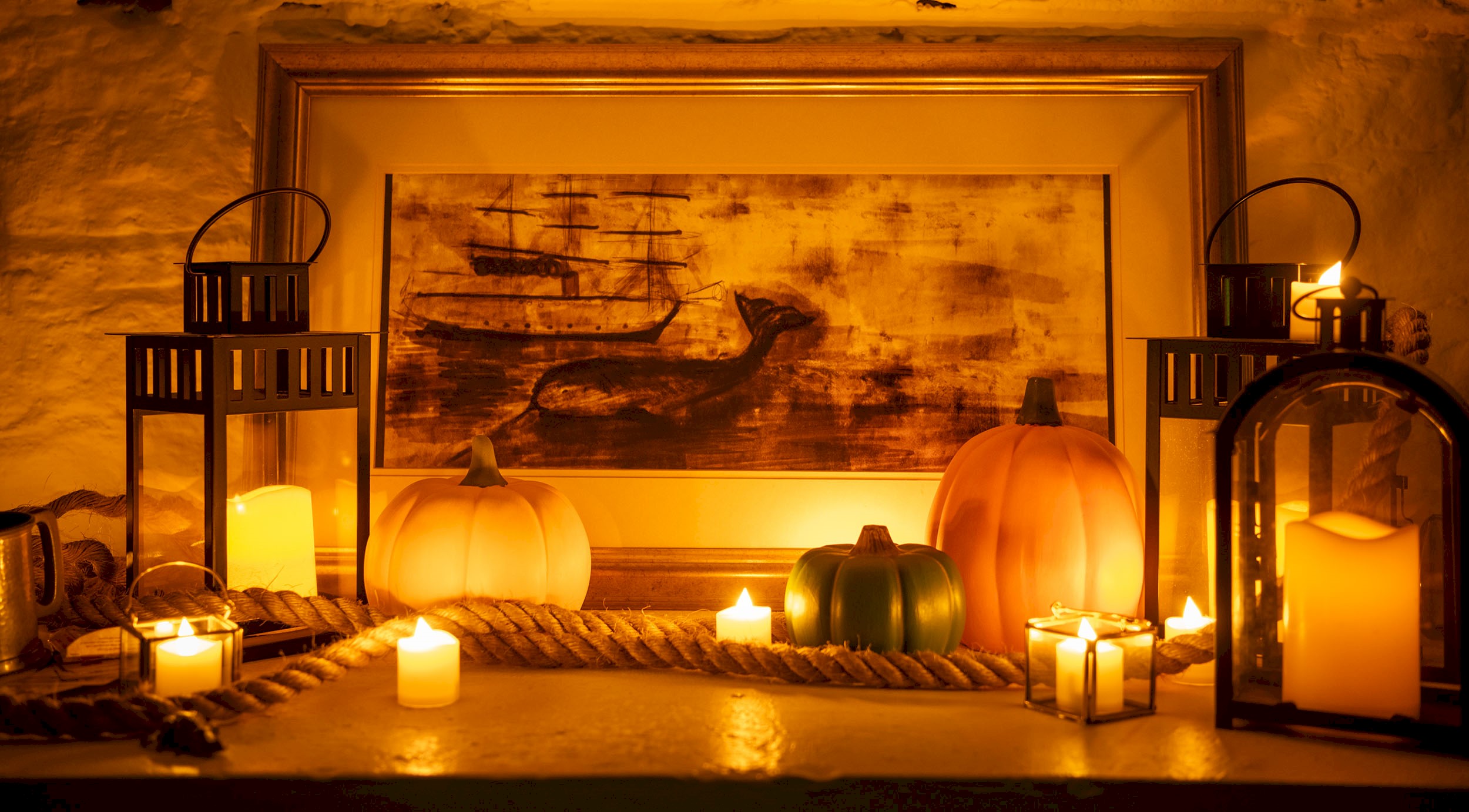 Lanterns with lit candles inside, small pumpkins, some rope and a picture of a ship with a whale 