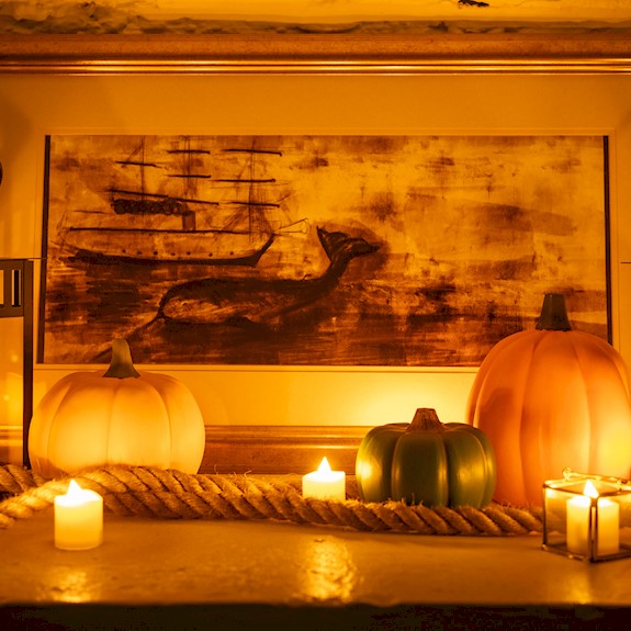Lanterns with lit candles inside, small pumpkins, some rope and a picture of a ship with a whale 