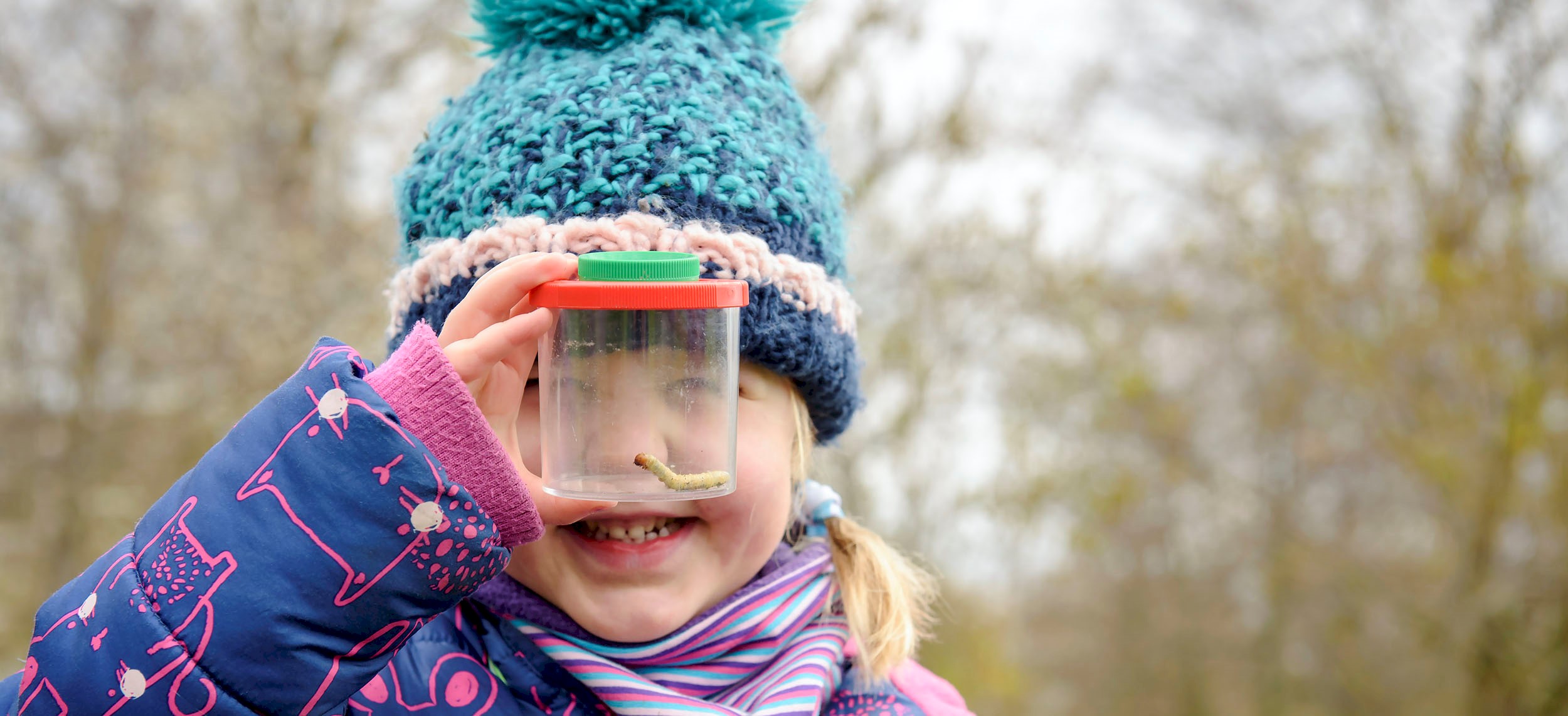 A girl with a hat on, looking at a worm in a tub