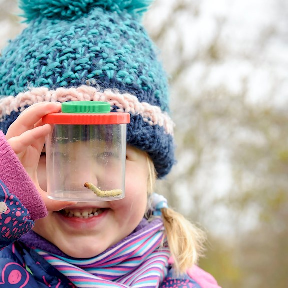 A girl with a hat on, looking at a worm in a tub