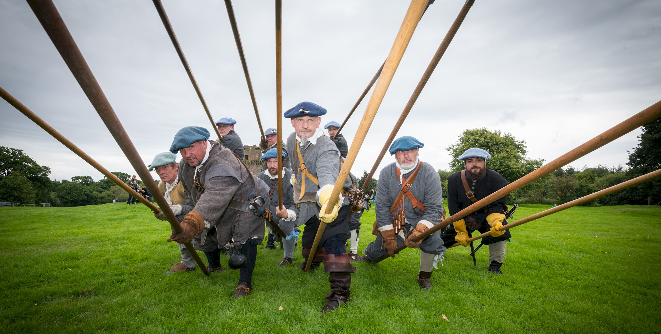 A group of costumed performers dressed as Covenanters leaning forward pointing pikes at the camera