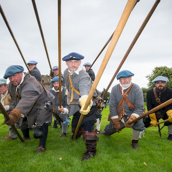 A group of costumed performers dressed as Covenanters leaning forward pointing pikes at the camera