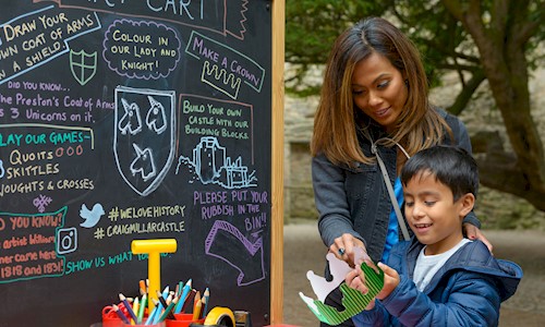 Lady and boy standing in front of a blackboard with lots of activities on it