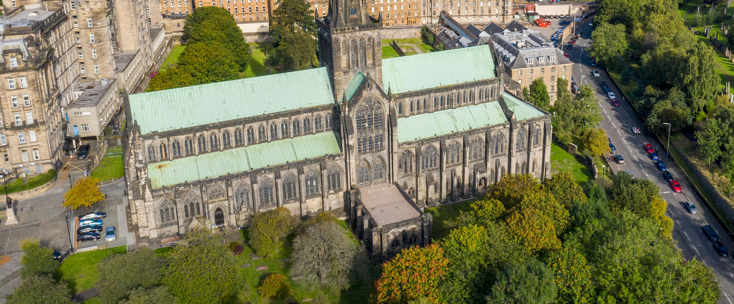 An aerial view of a cathedral on a sunny day. You can see buildings in the surrounding area, as well as green spaces nearby. 