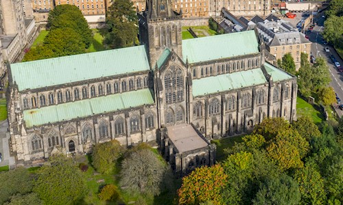 An aerial view of a cathedral on a sunny day. You can see buildings in the surrounding area, as well as green spaces nearby. 