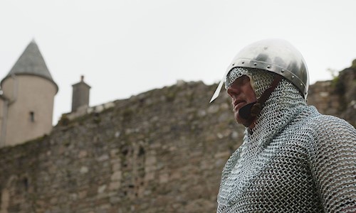 A costumed performer wearing chainmail and a helmet in the grounds of a castle