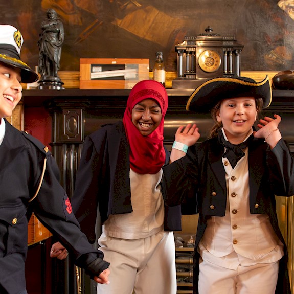 Four children dressed up in maritime regalia smiling with their hands in the air