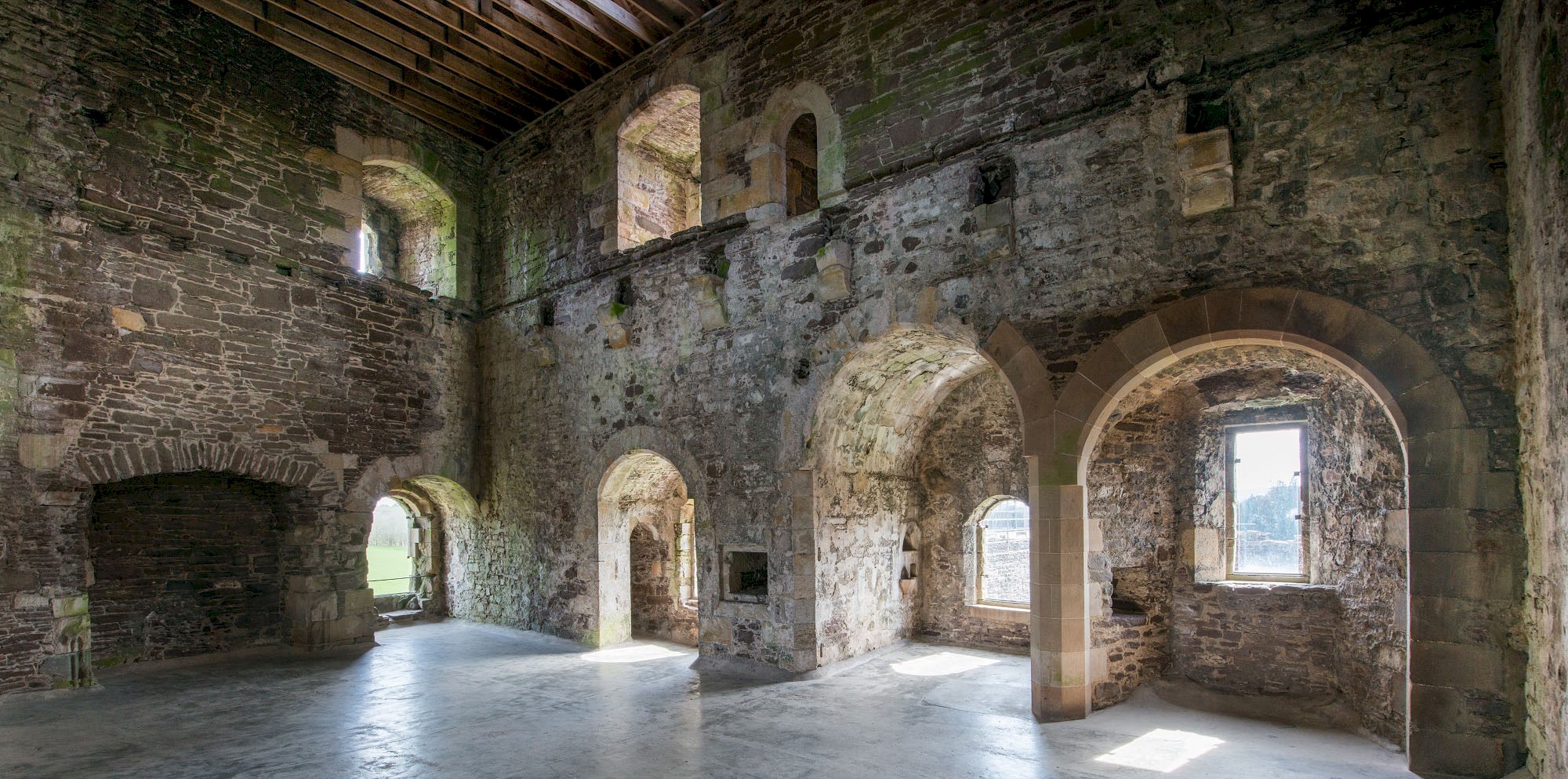 Interior view of a great hall in a castle with a fireplace and many arches and windows 
