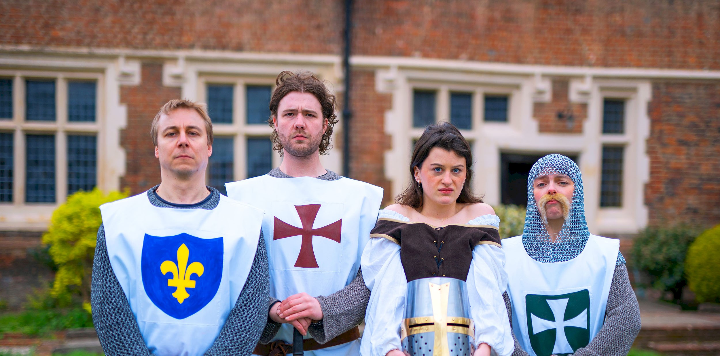 Four people in historical costume for different 'teams' standing in a line looking nonplussed