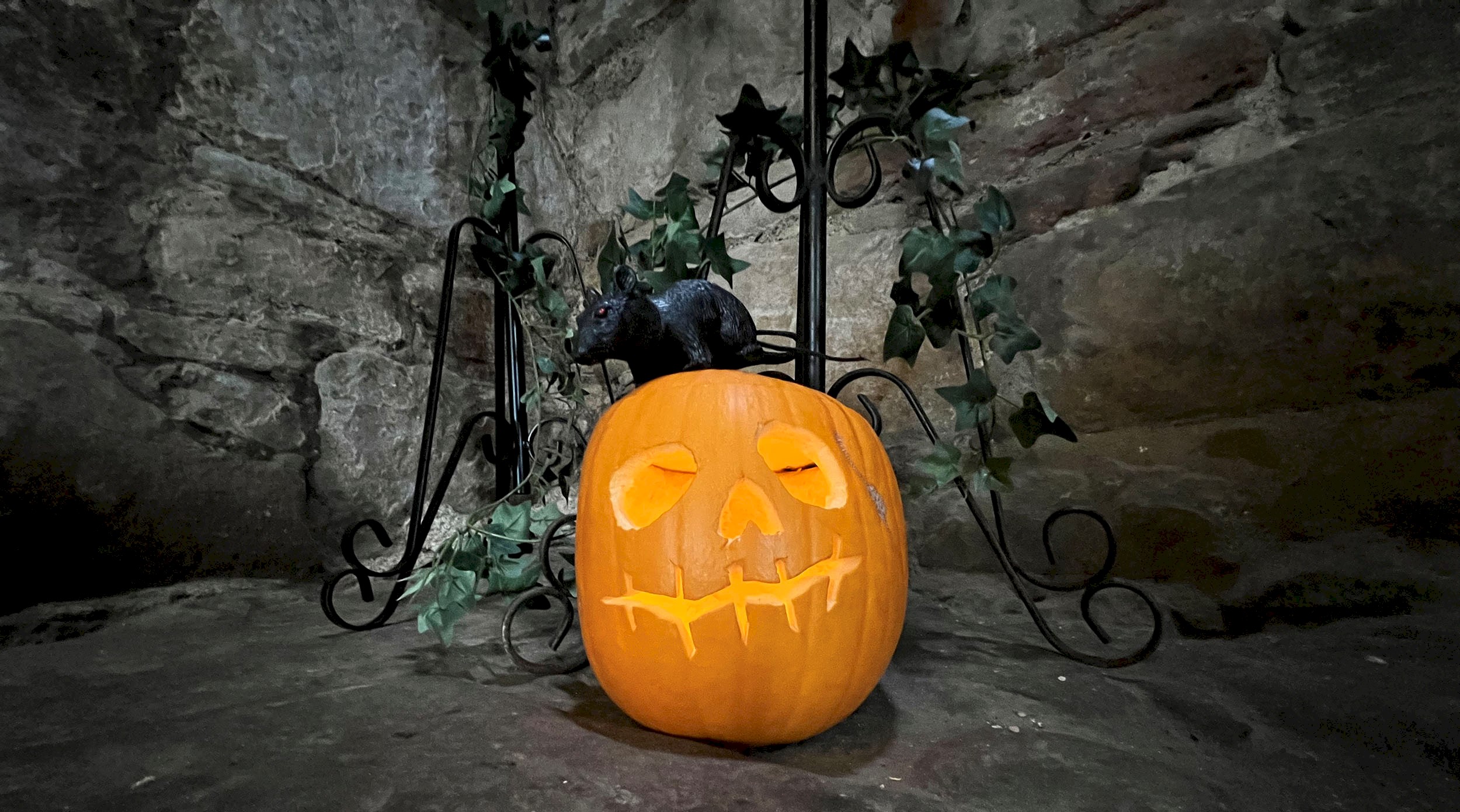 A carved pumpkin surrounded with ivy leaves and a pretend rat sitting on top of it