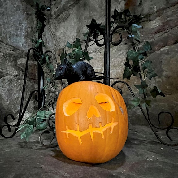 A carved pumpkin surrounded with ivy leaves and a pretend rat sitting on top of it