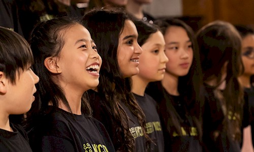 A group of young people wearing tshirts saying NYCOS smiling and singing