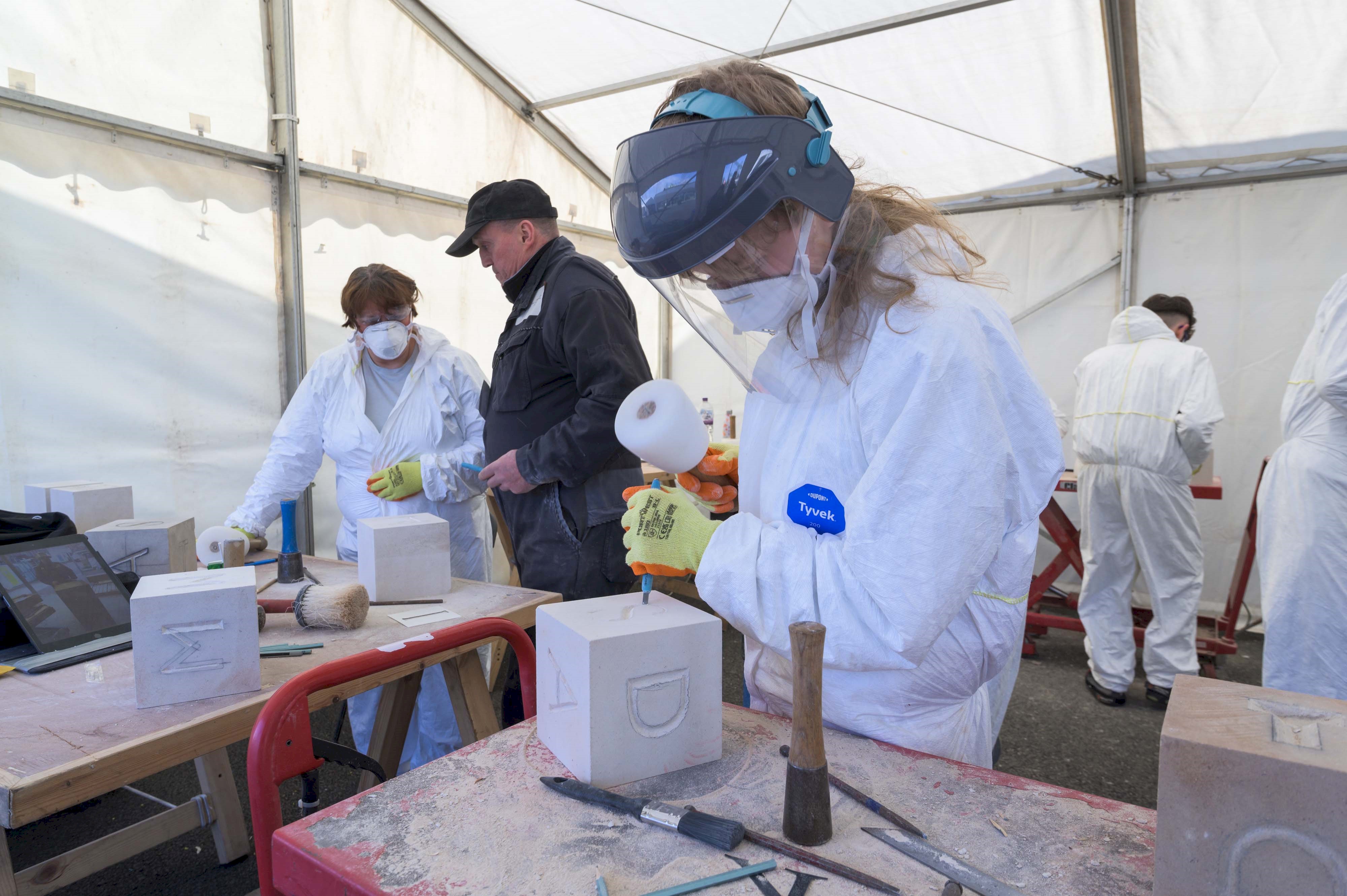 A person carving a letter into a block of stone in a marquee