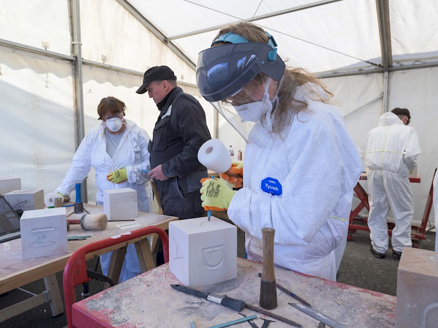 A person carving a letter into a block of stone in a marquee