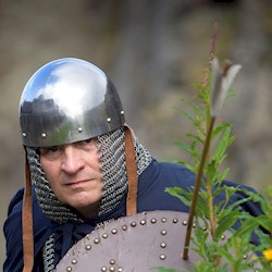 A costumed performer wearing chainmail holding a shield with an arrow fired into it