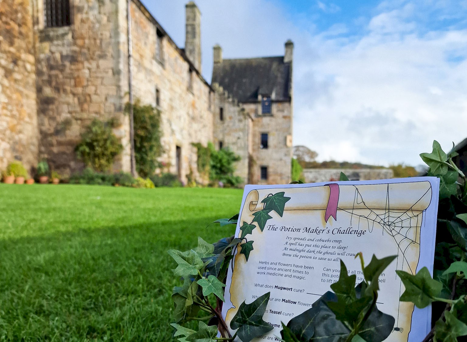 A sign on a grass lawn with ivy draped over it and a castle in the background